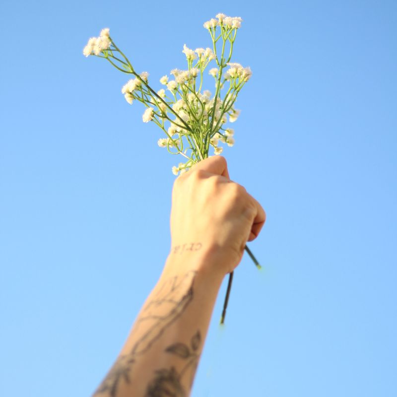 Main avec phrase tatouée tenant un bouquet de fleur