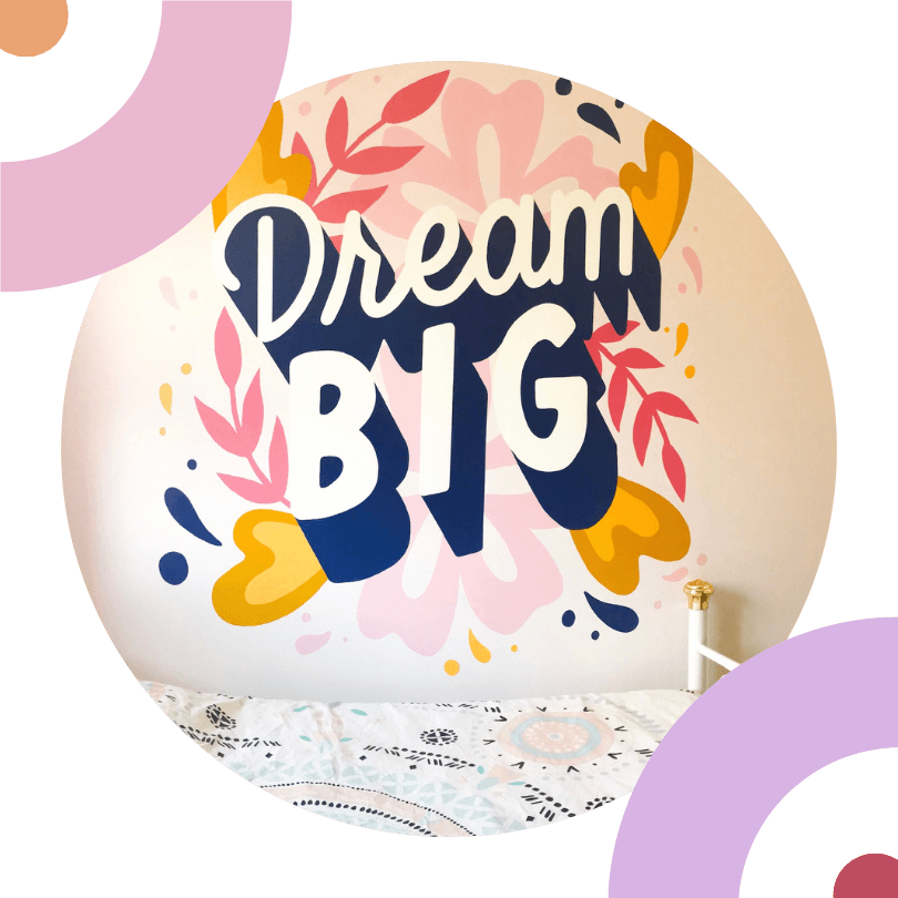 Fresque murale "Dream Big" en blanc et bleu avec des feuilles en rose et rouge et jaune autour.
